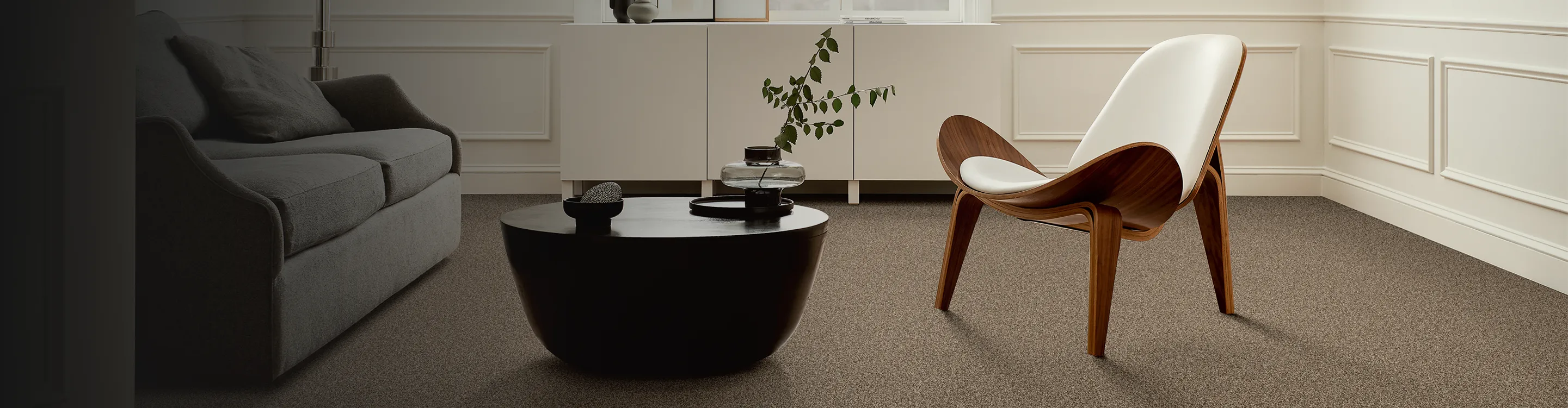beige carpet flooring in contemporary living room with black coffee table, modern wood chair and abstract art